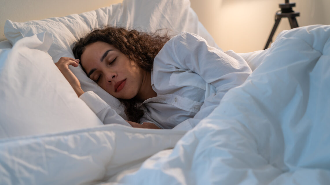 Latino beautiful woman lying down on bed in bedroom in dark night room.